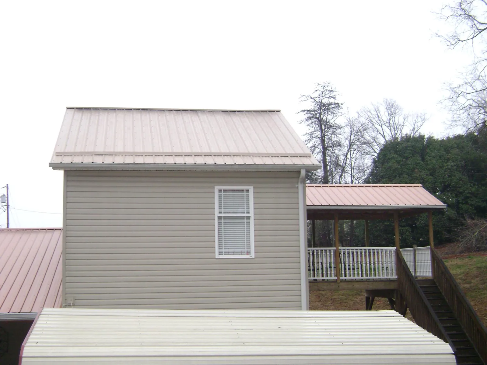 Tan metal roofs on a two story addition and attached porch, from a Roof Replacement job in Worcester